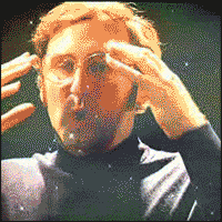 A gif of a guy moving his hands away from his forehead as a circle of light/stars/galaxy pattern expands around him.